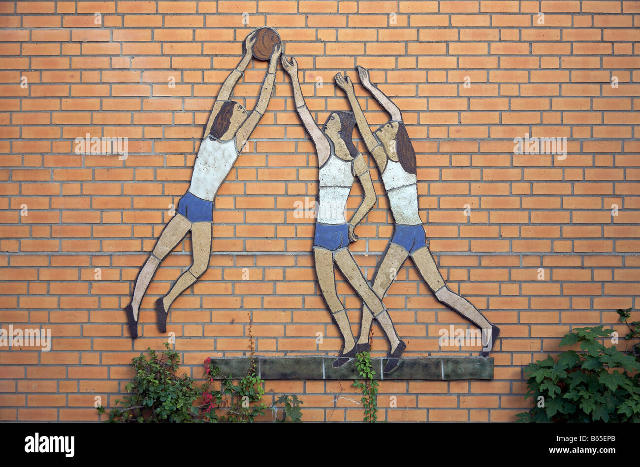 Kachelplastik mit 3 ballspielenden Frauen auf der Gebäudefront einer Turnhalle mural of handball playing girls on a facade Stock Photo