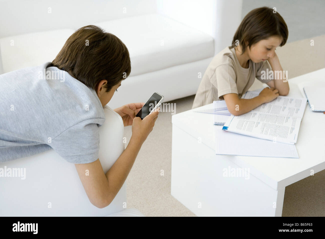Boy reading at coffee table, brother leaning on armchair, holding cell phone Stock Photo Alamy