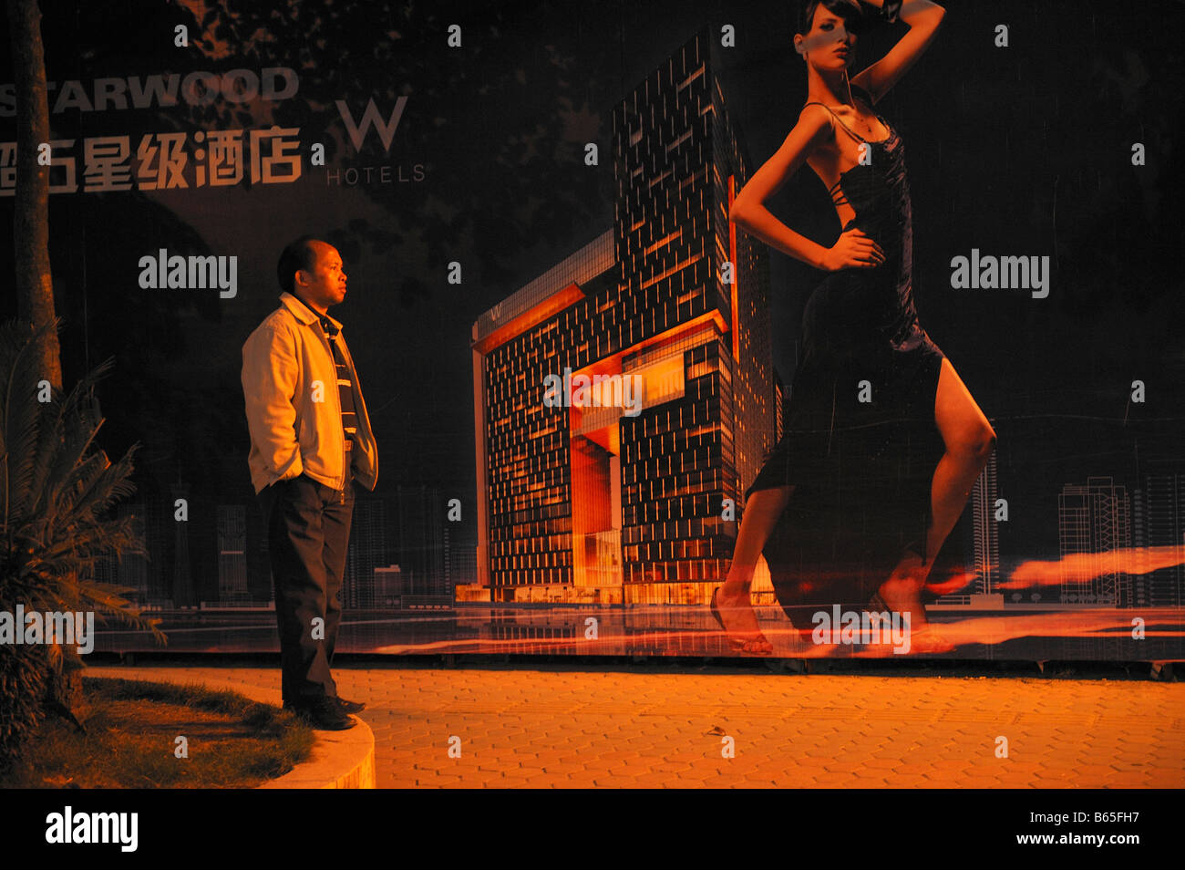 A Chinese migrant worker stands in front of a billboard featuring a luxurious hotel being built in Guangzhou. 26-Nov-2008 Stock Photo