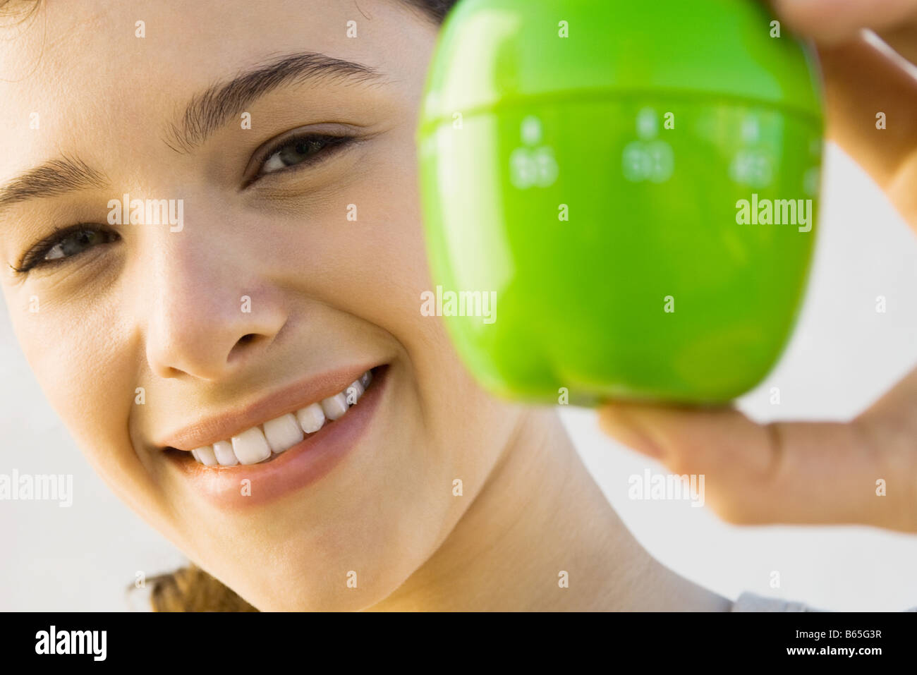 Woman holding up kitchen timer, smiling at camera, focus on background Stock Photo