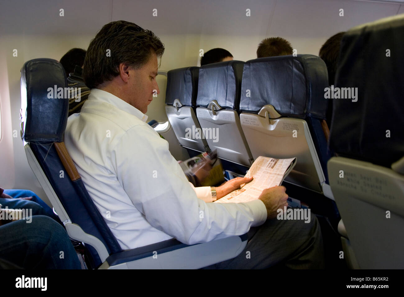 Airline passenger reads newspaper in his seat Stock Photo
