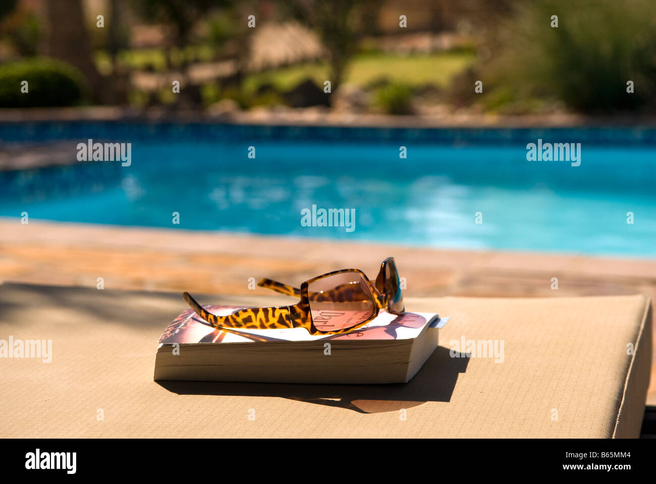 A book and sun glasses by the pool ready for a relaxing holiday read ...