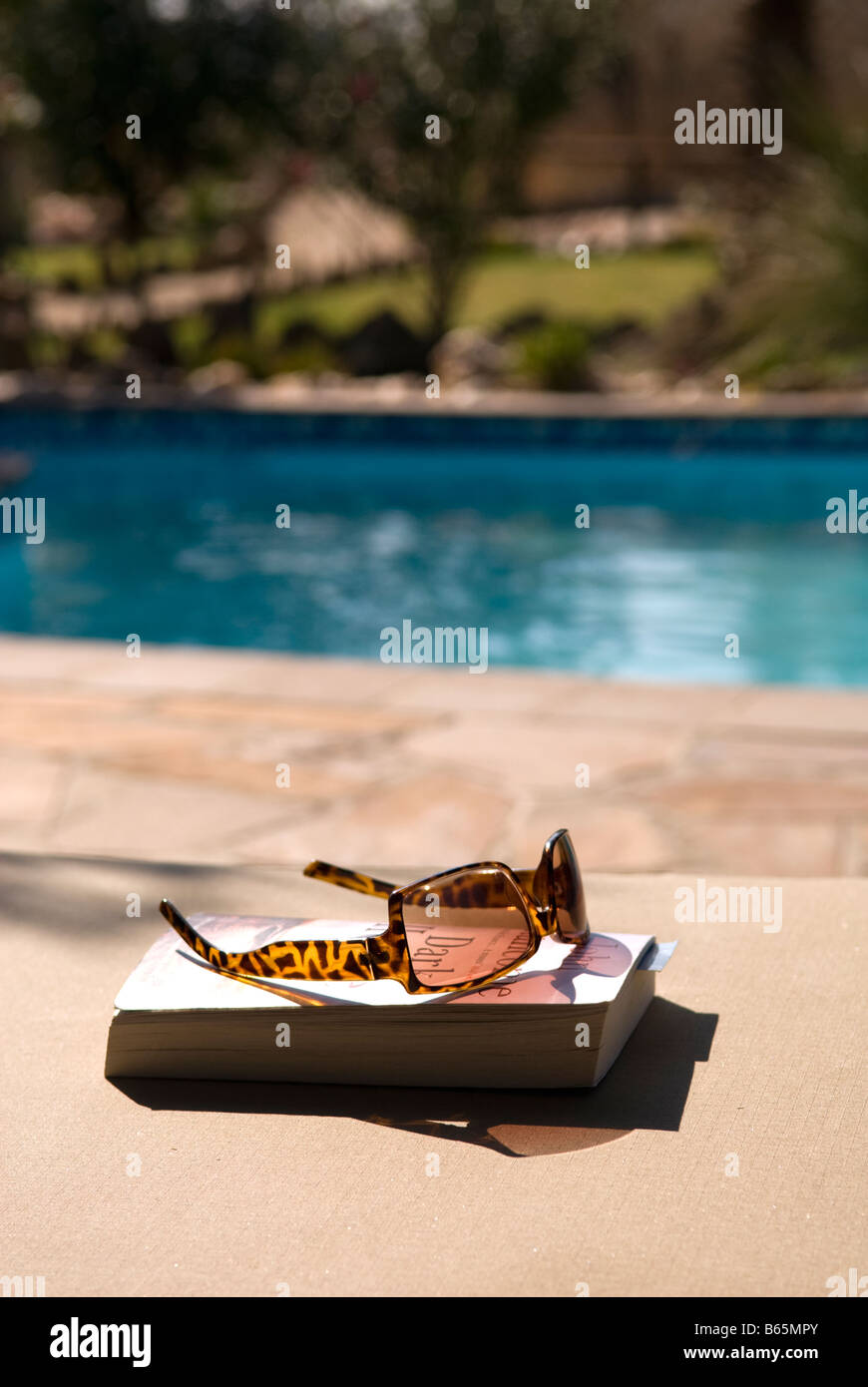 A book and sun glasses by the pool ready for a relaxing holiday read ...