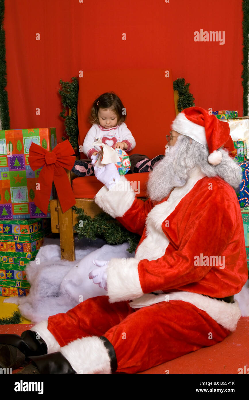 Santa Claus opening christmas gift with a 2 year old little girl Stock