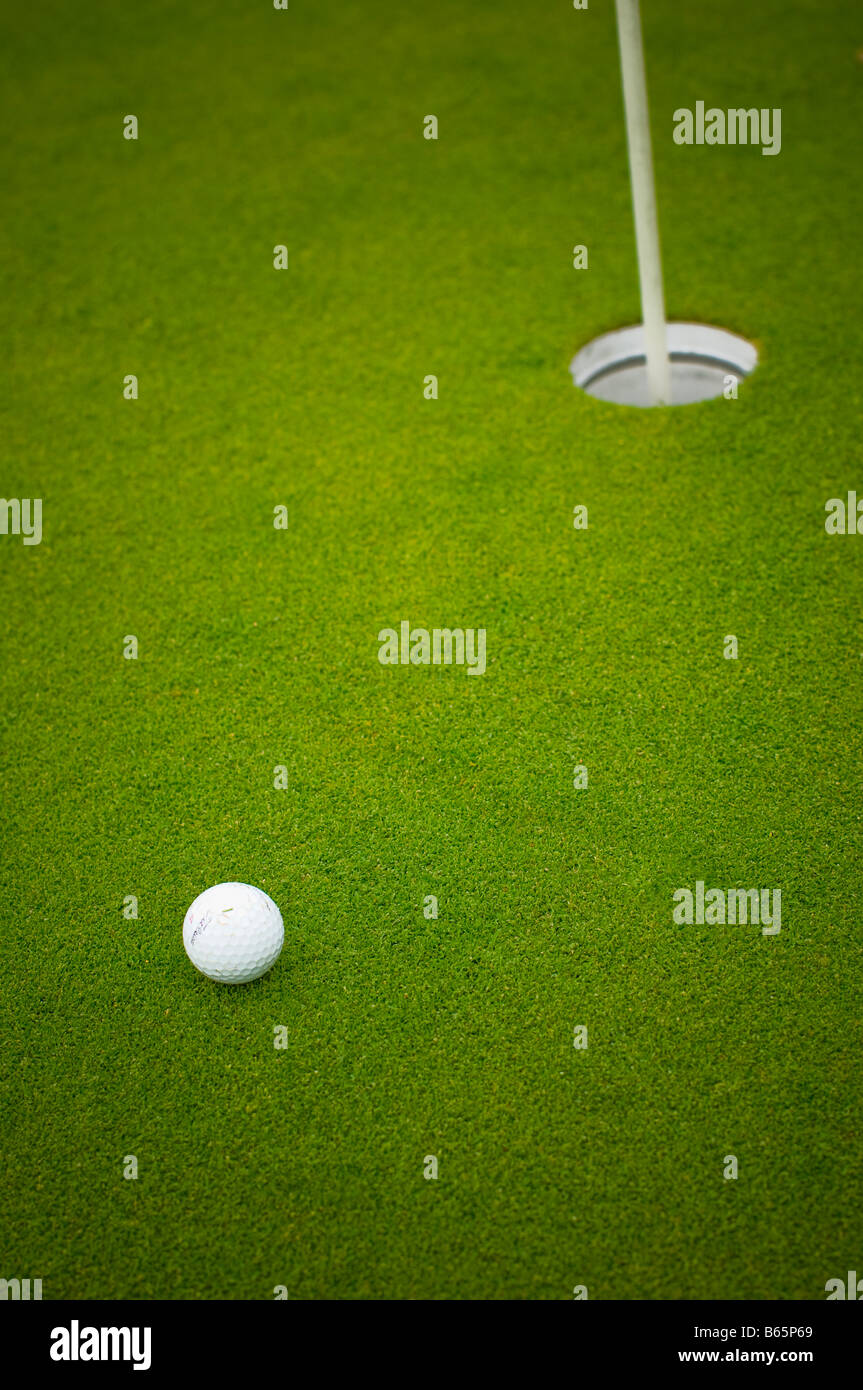 Golf ball near the cup on the green. Stock Photo