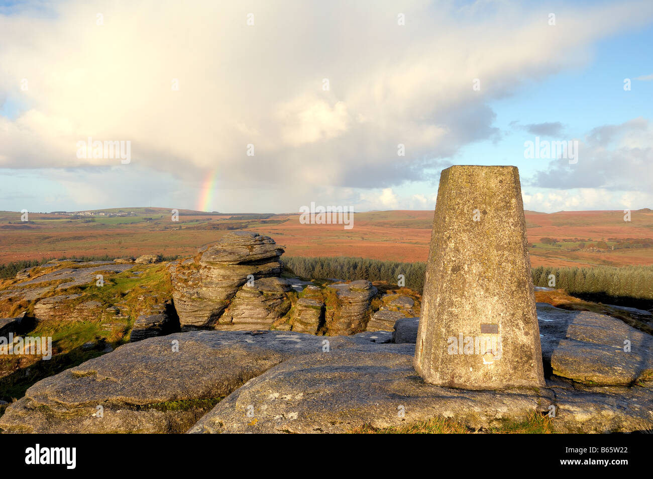 Early morning light and a rainbow at Bellever Tor on Dartmoor in South Devon UK with the triangulation pillar on the summit Stock Photo
