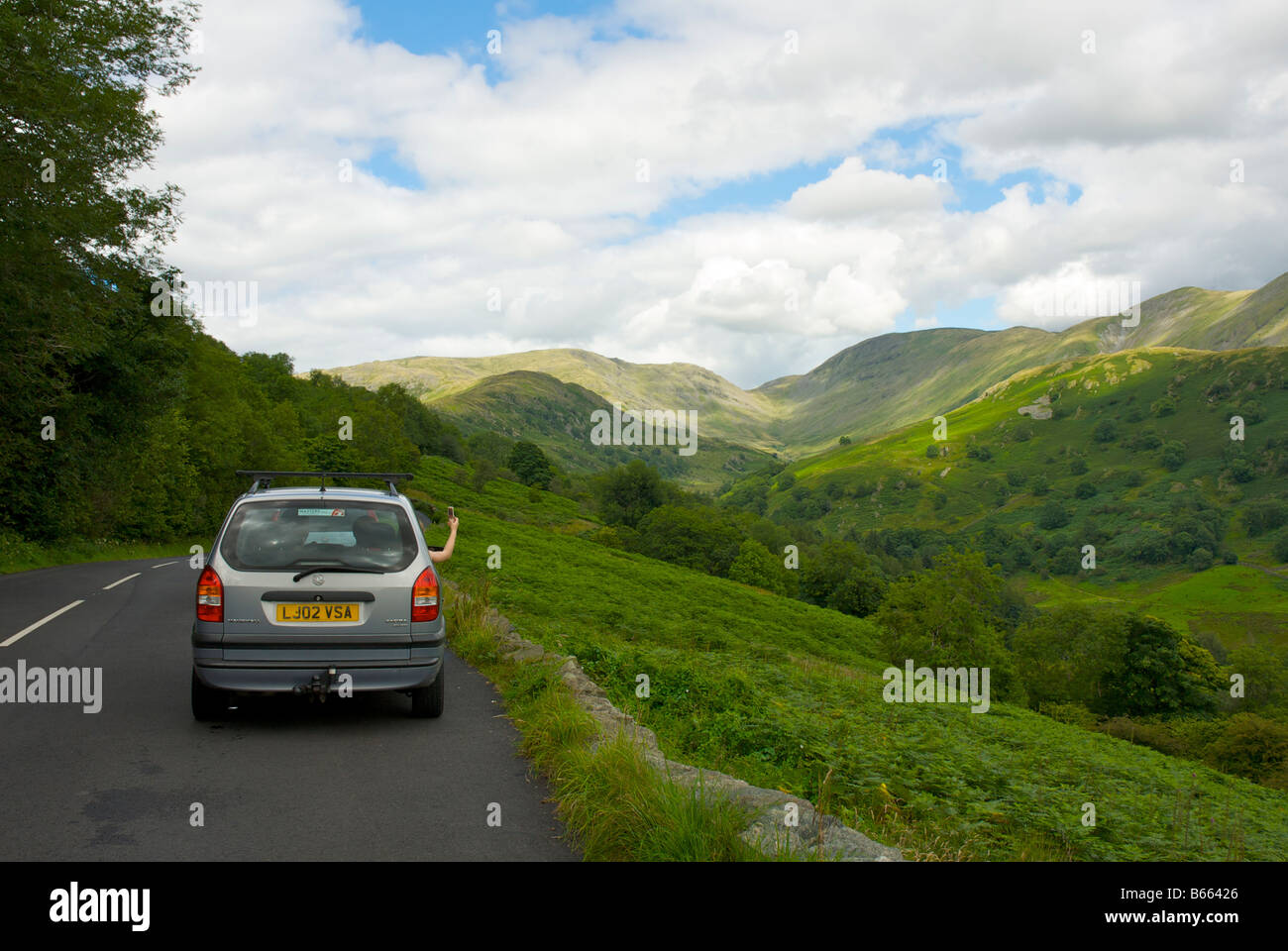Car driver taking photograph of Troutbeck Valley on phone without