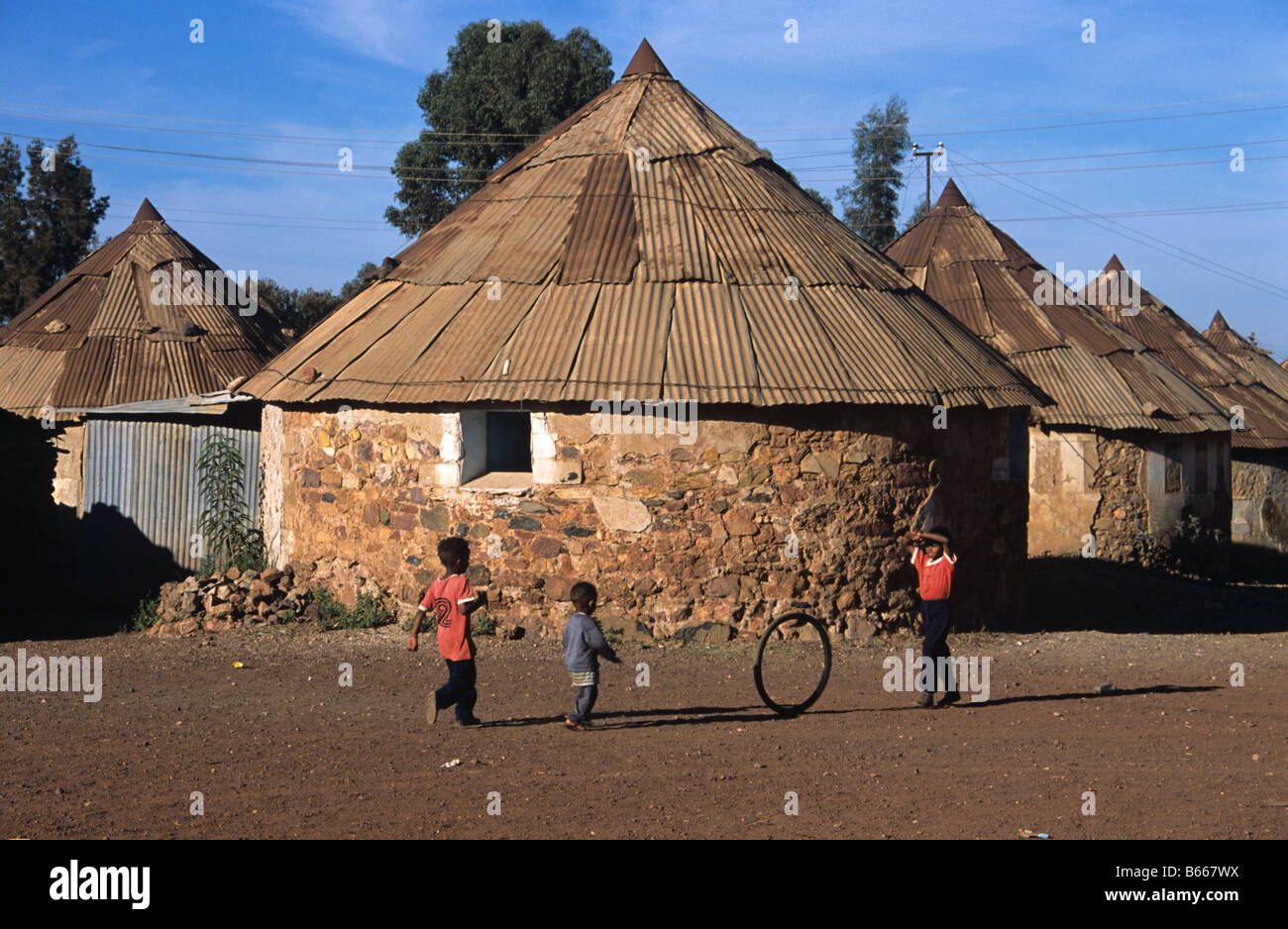 Eritrean boys playing with a hoop or bicycle tyre outside their round house or hut, Asmara, Eritrea Stock Photo