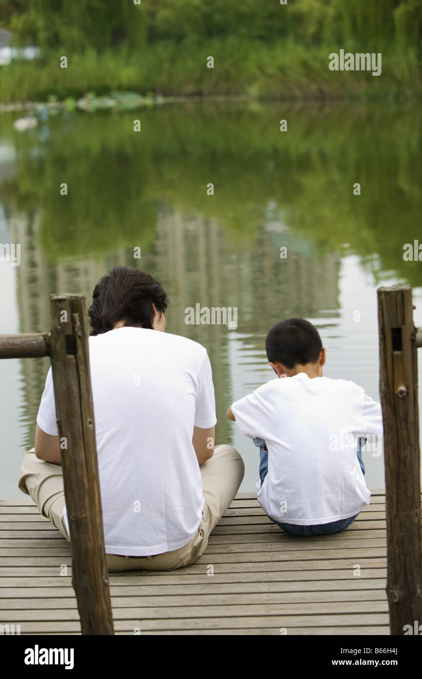 Young father with son sitting on the wooden board near the lakeside Stock Photo