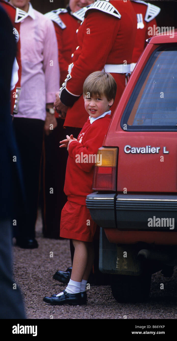 A young Prince William wearing red shorts and a red sweatshirt leaning against a red car guardsman in the background Stock Photo