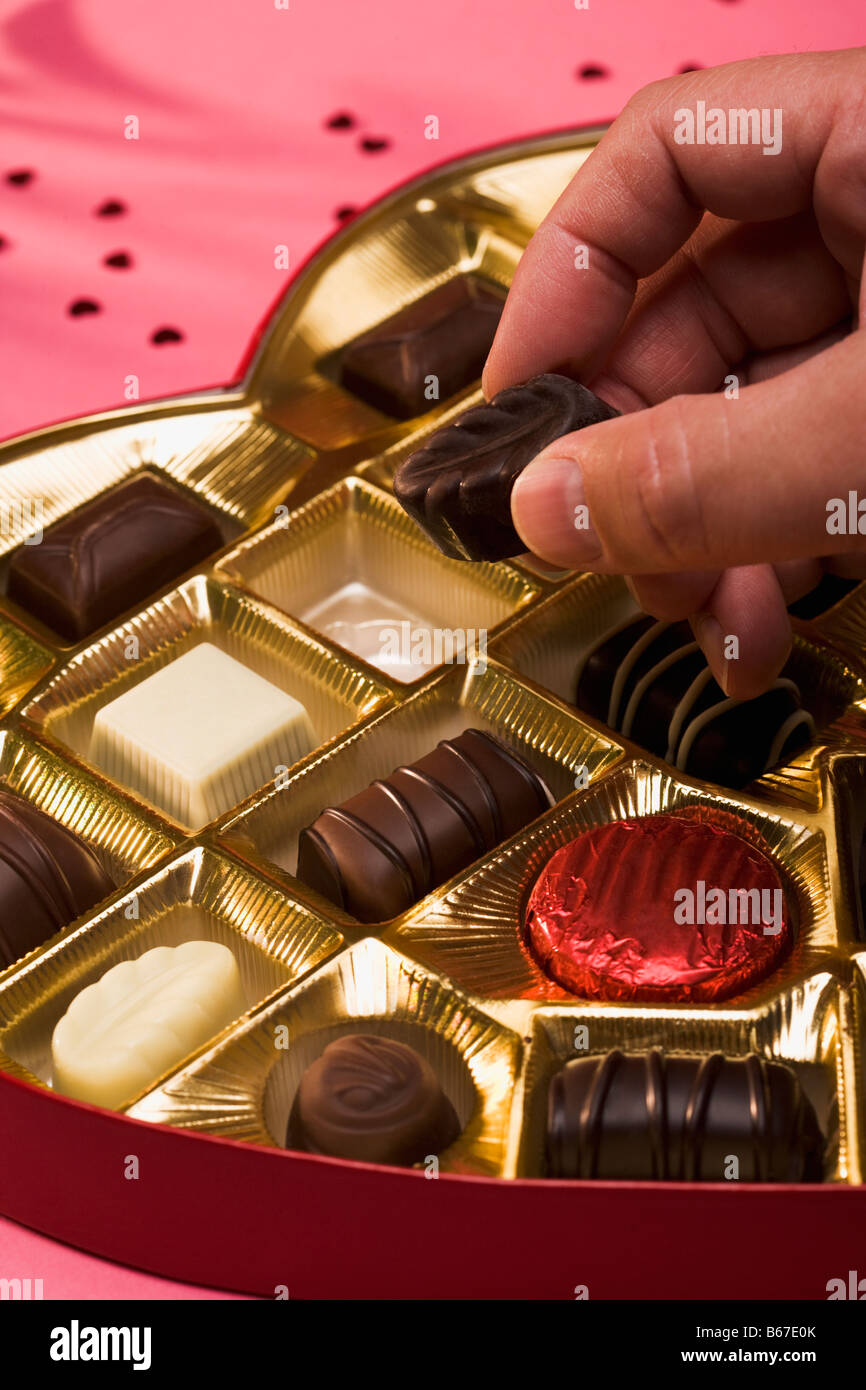 Man's hand taking chocolate piece from heart shaped box Stock Photo