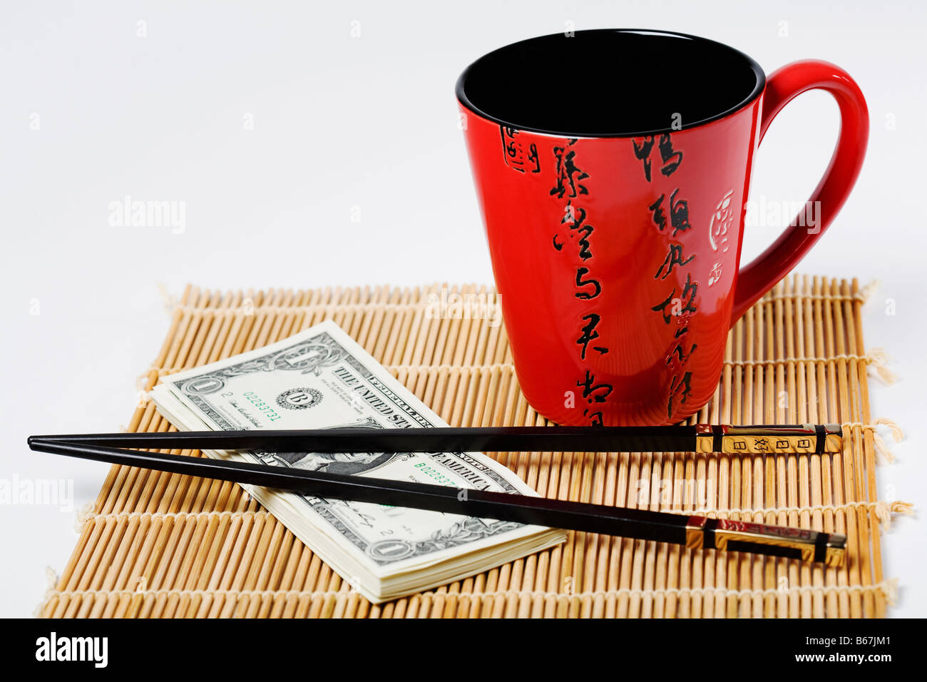 Chopsticks with a stack of US paper currency and a cup on place mat Stock Photo