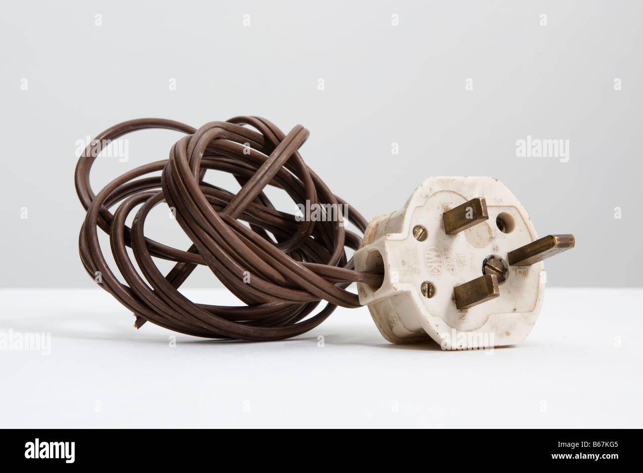 old white , UK standard 13 amp electrical plug and coil of brown flex Stock Photo
