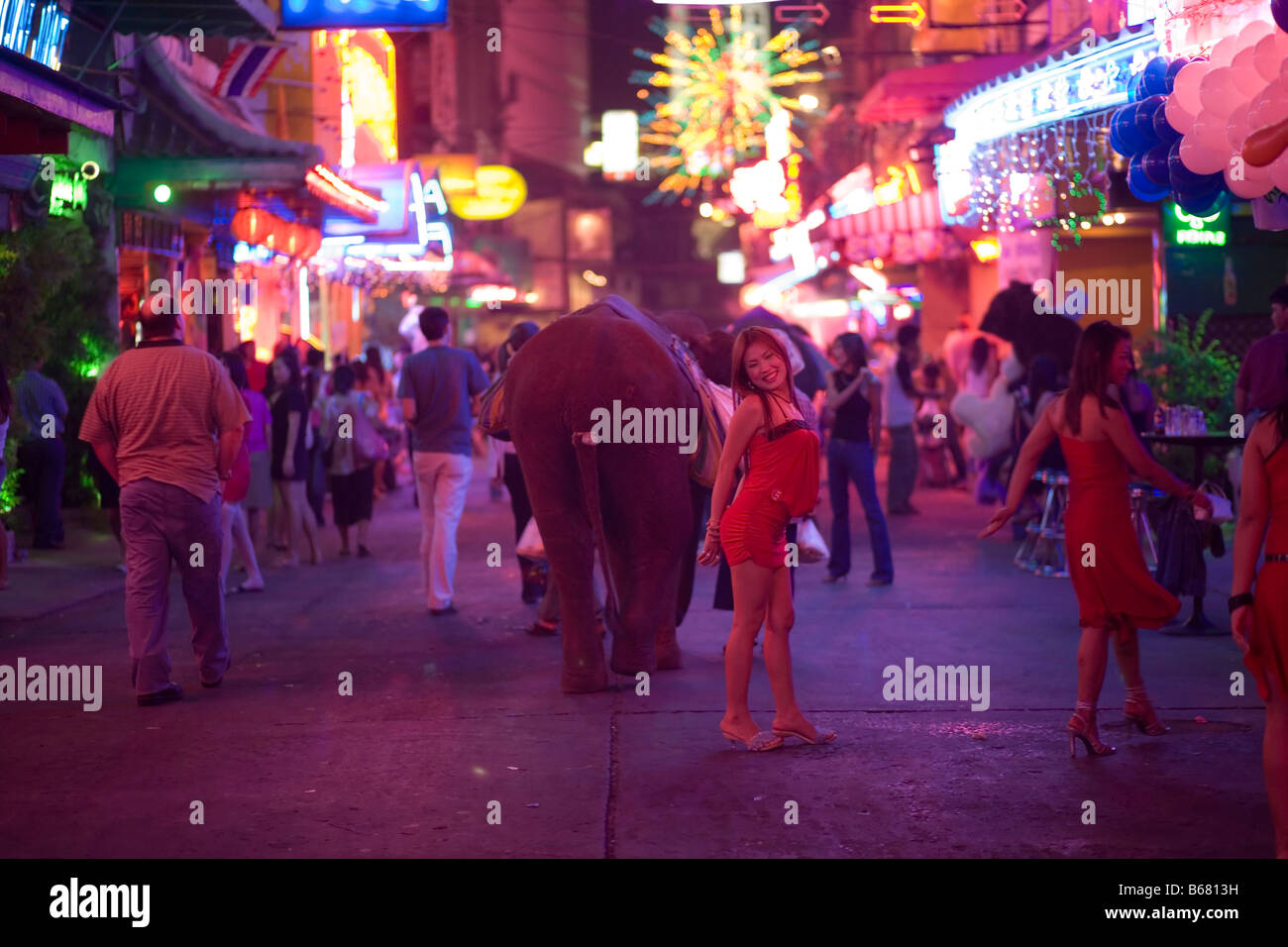 People strolling over Soi Cowboy with bars and nightclubs, red-light district, woman smiling at camera in foreground, Th Sukhumv Stock Photo