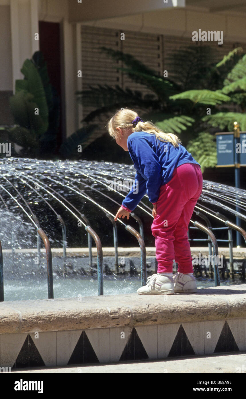 Girl plays with water jets in public fountain. Stock Photo