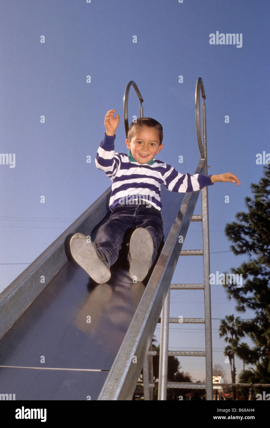 Hispanic boy glides down metal playground slide. Stock Photo