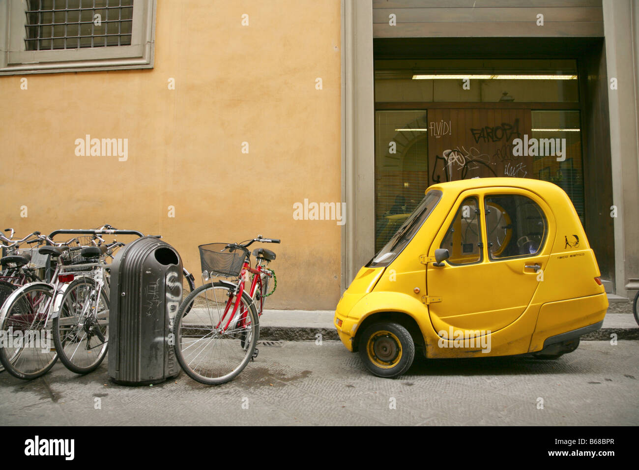 Bicycles and small yellow one-person electric Pasquali Riscio car parked in sidestreet, Florence, Italy. Stock Photo