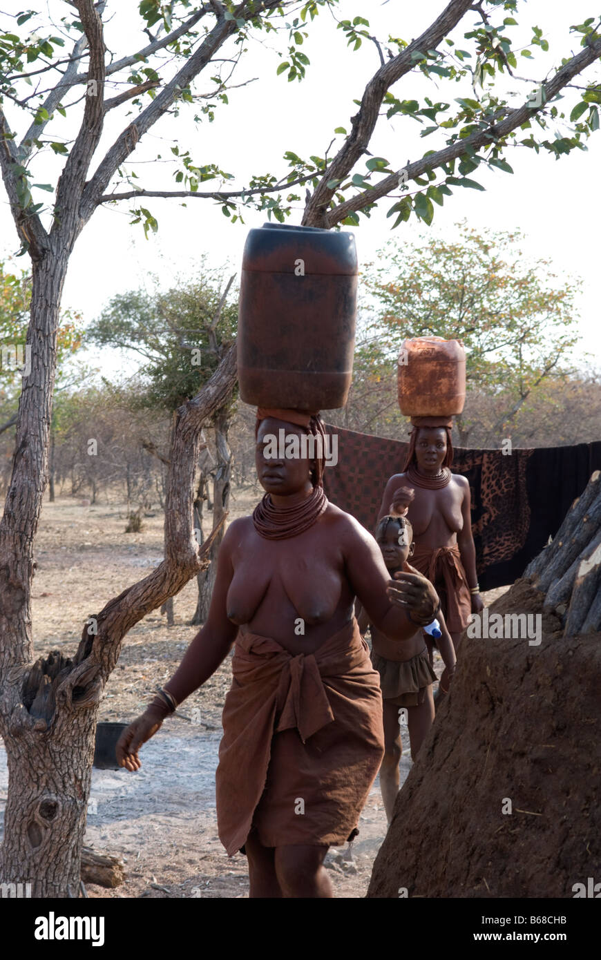 Himba women carry barrels of water on their heads at the Himba Oase Village near Kamanjab, Namibia Stock Photo