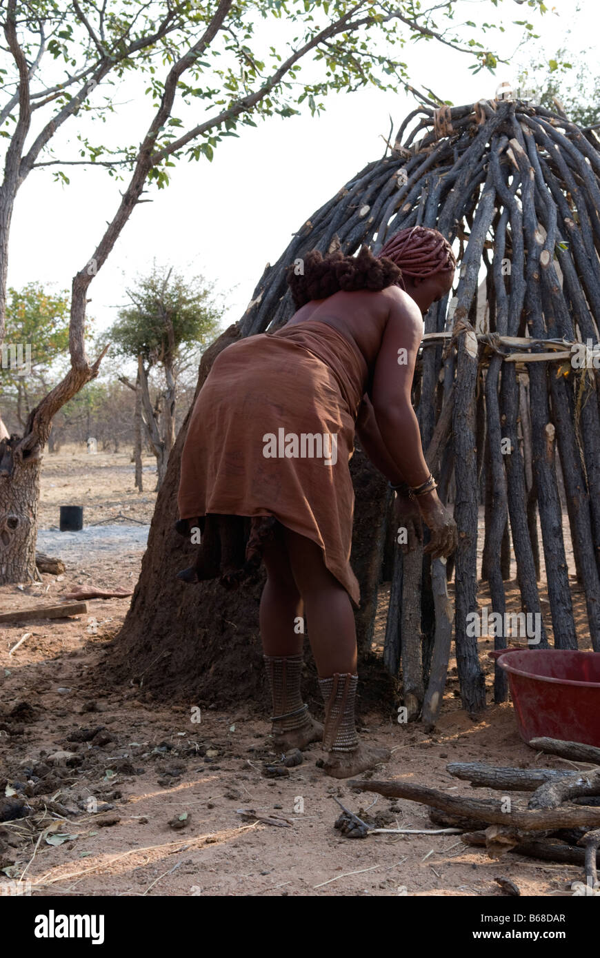 A young woman builds a traditionall village hut from sticks mud and dung at the Himba Oase Village near Kamanjab Namibia Africa Stock Photo