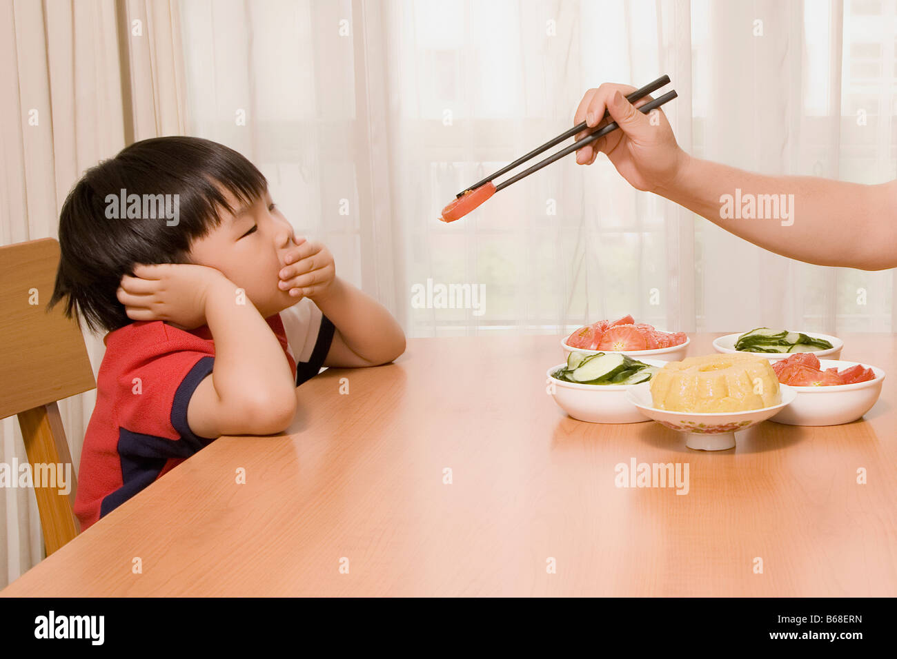 Person's hand holding chopsticks and feeding a boy Stock Photo