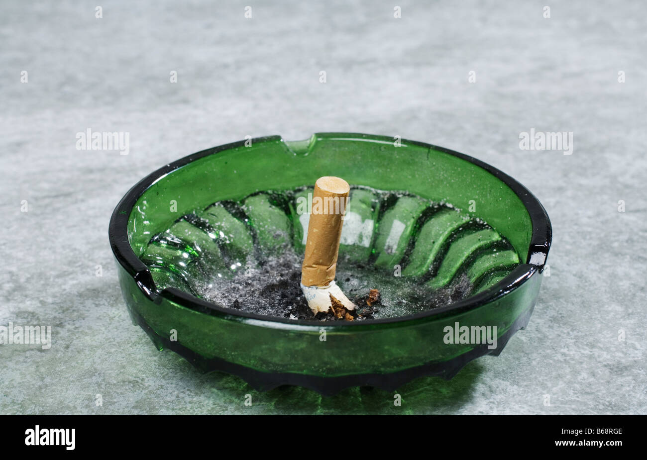 A cigarette butt stubbed out in a green glass ashtray Stock Photo
