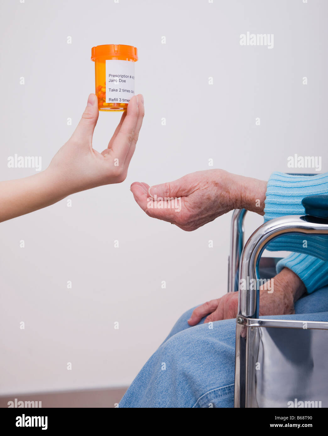 Young woman giving pill bottle to senior woman, close-up of hands Stock Photo