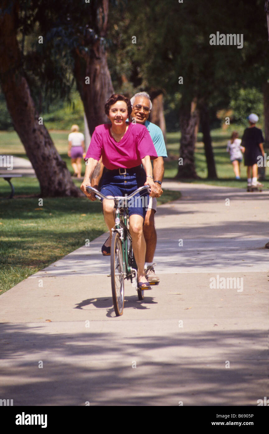 Hispanic couple ride tandem bike in park. Stock Photo
