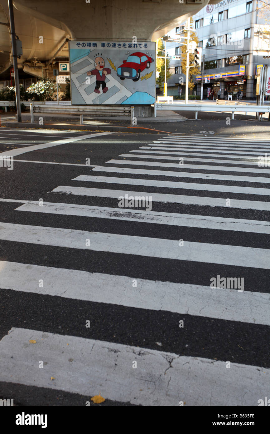 A pedestrian zebra crossing in Meiji Jingumae Tokyo with a cartoon warning pedestrians of being run over by a car Stock Photo