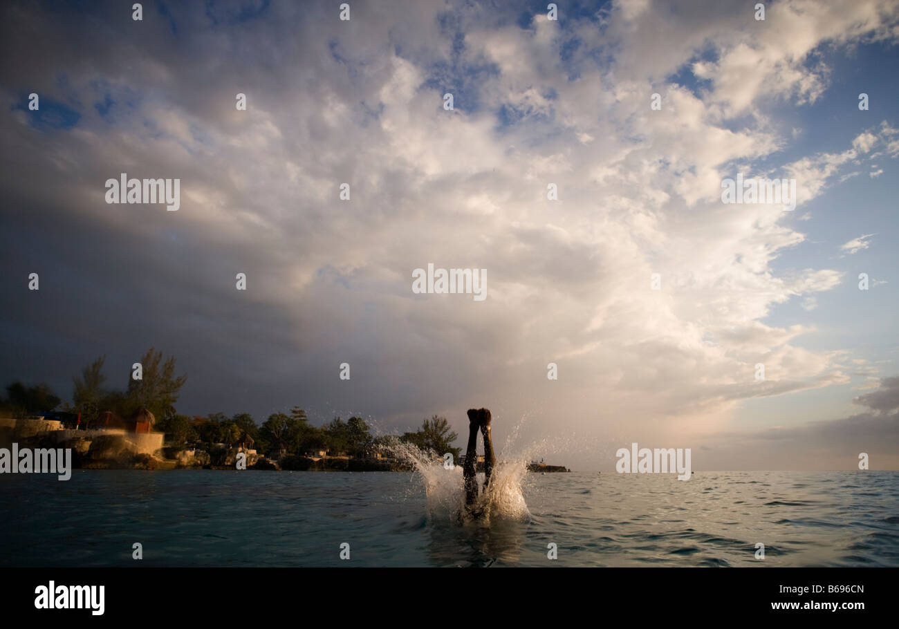 Jamaica Negril Silhouette of young man leaping from from cliff above Pirates Cave Stock Photo