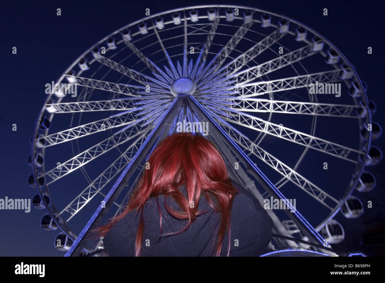 woman with red hair looking up at a ferris wheel in hyde park london Stock Photo
