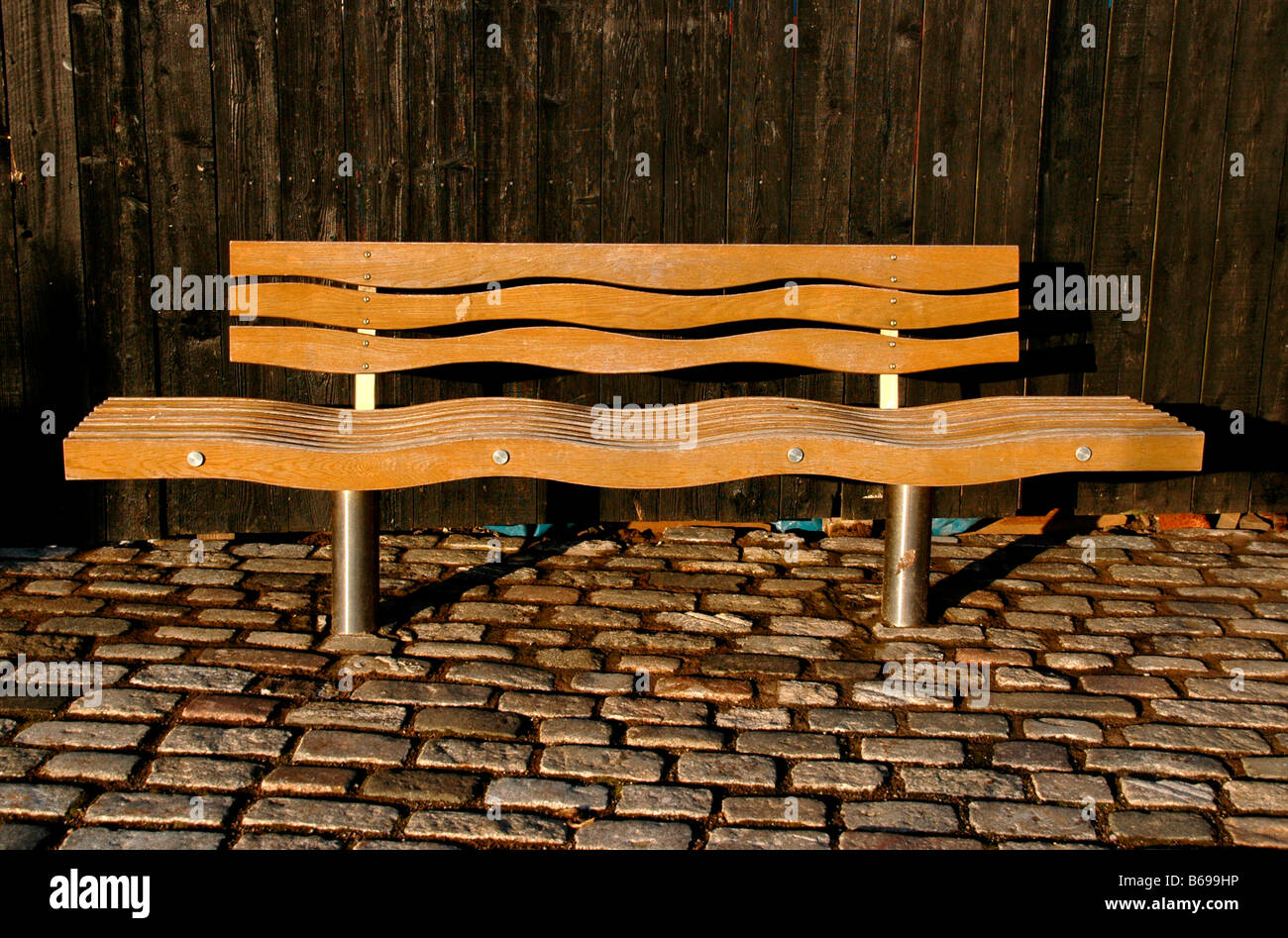 A wooden public bench at a harbour. The wavy shapes of it evoking the sea. Stock Photo
