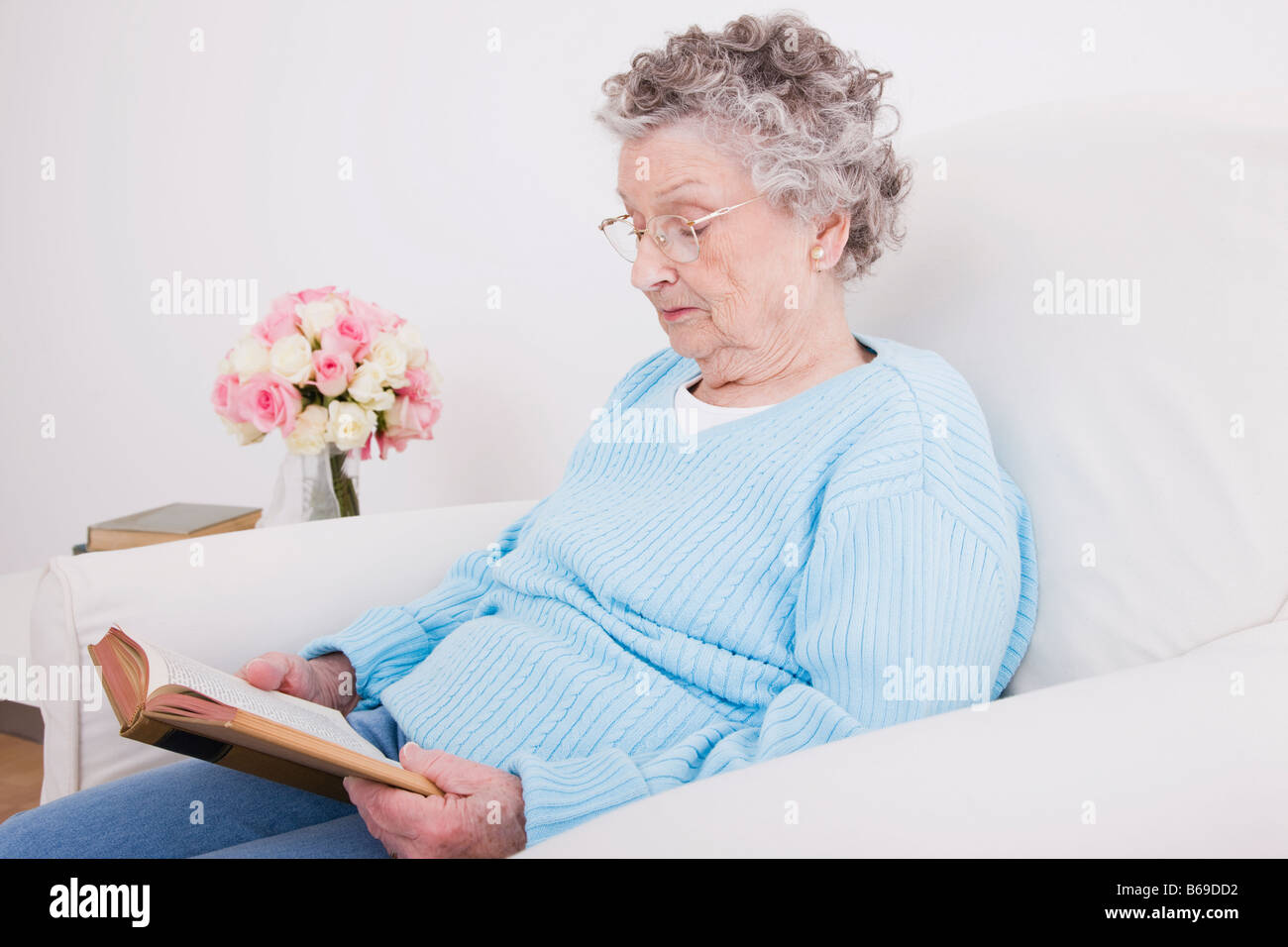 Senior woman sitting in armchair and reading book Stock Photo - Alamy