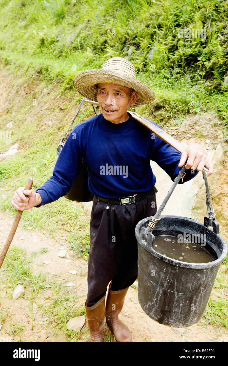Senior man carrying a bucket full of water on his shoulder, Jinkeng