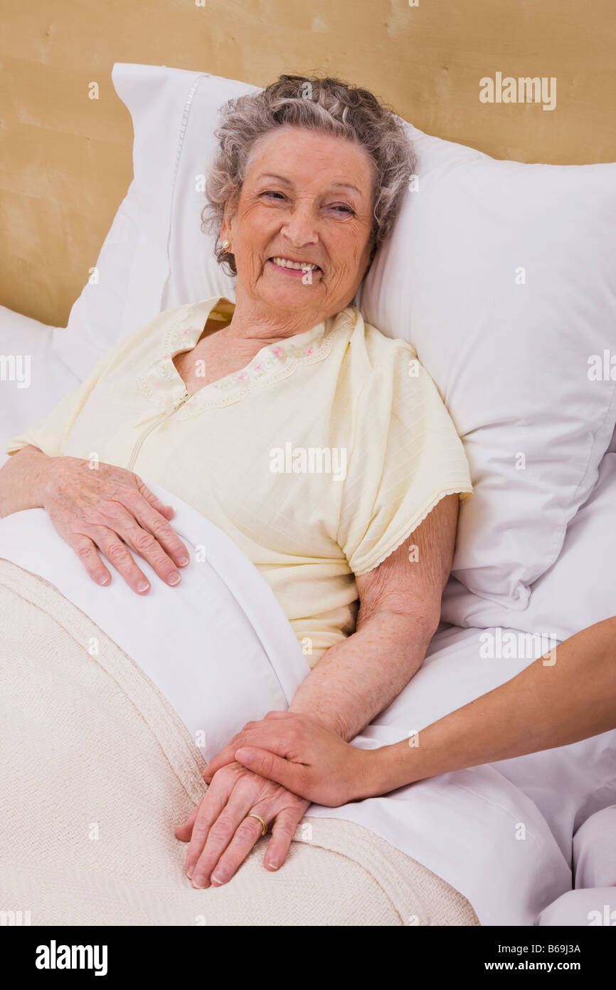 Woman holding senior woman's hand on bed Stock Photo