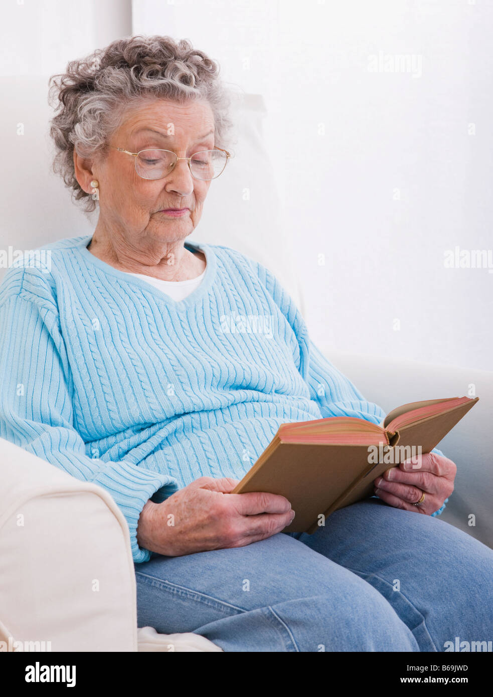 Senior woman sitting in armchair and reading book Stock Photo - Alamy