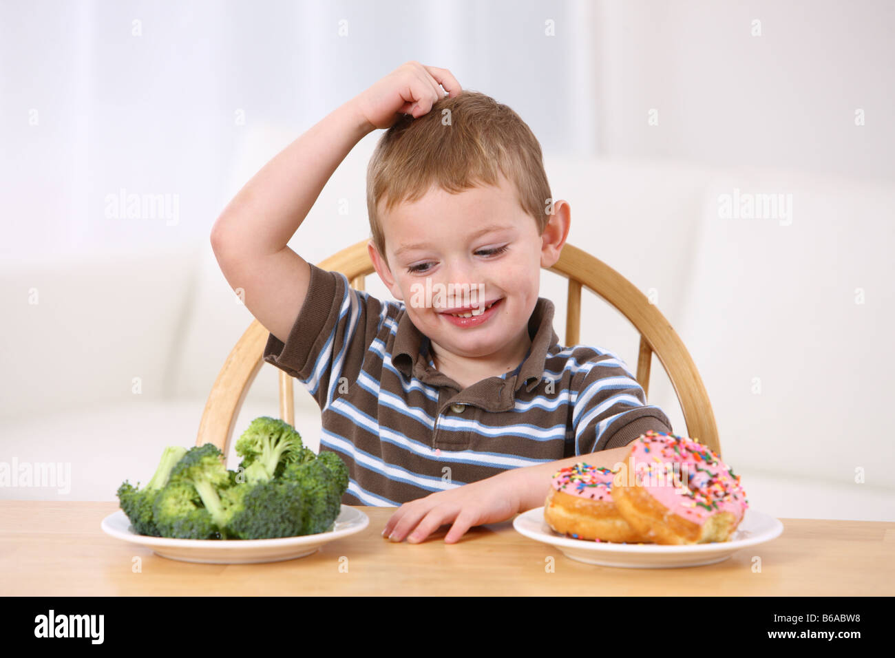 Young boy making choice between broccoli and doughnuts Stock Photo