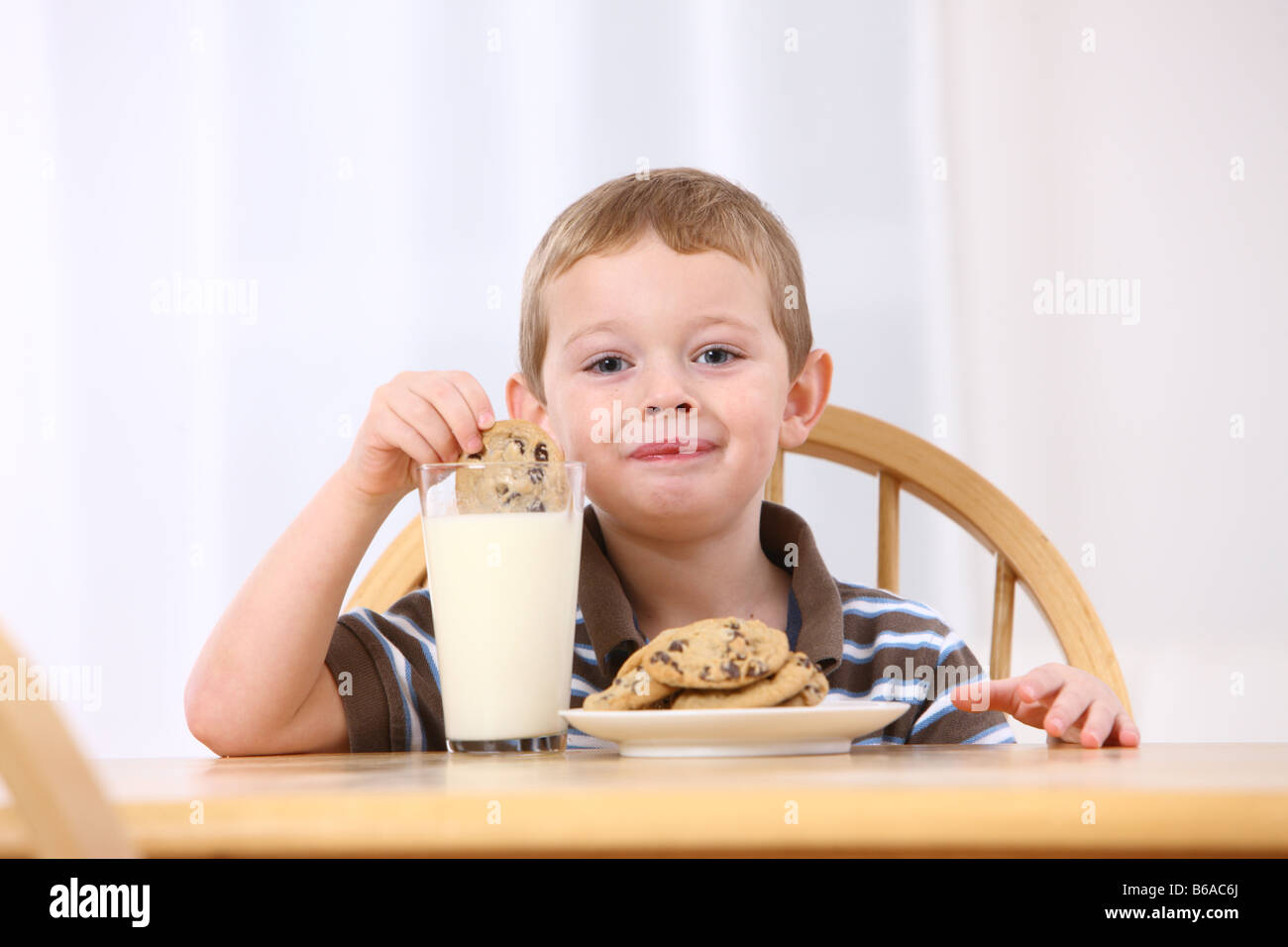 Young boy putting cookie in milk Stock Photo