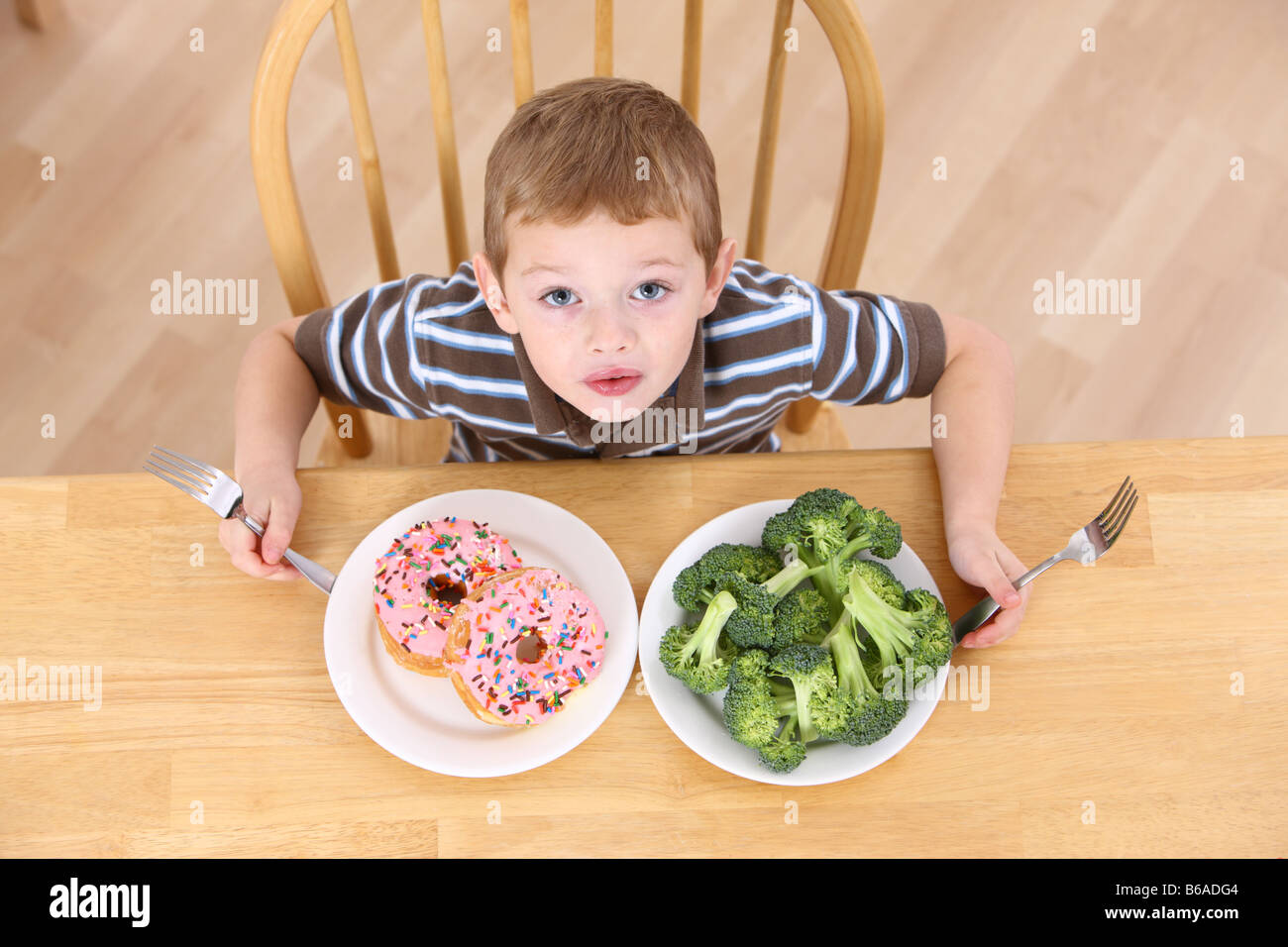 Young boy with plates of broccoli and doughnuts Stock Photo