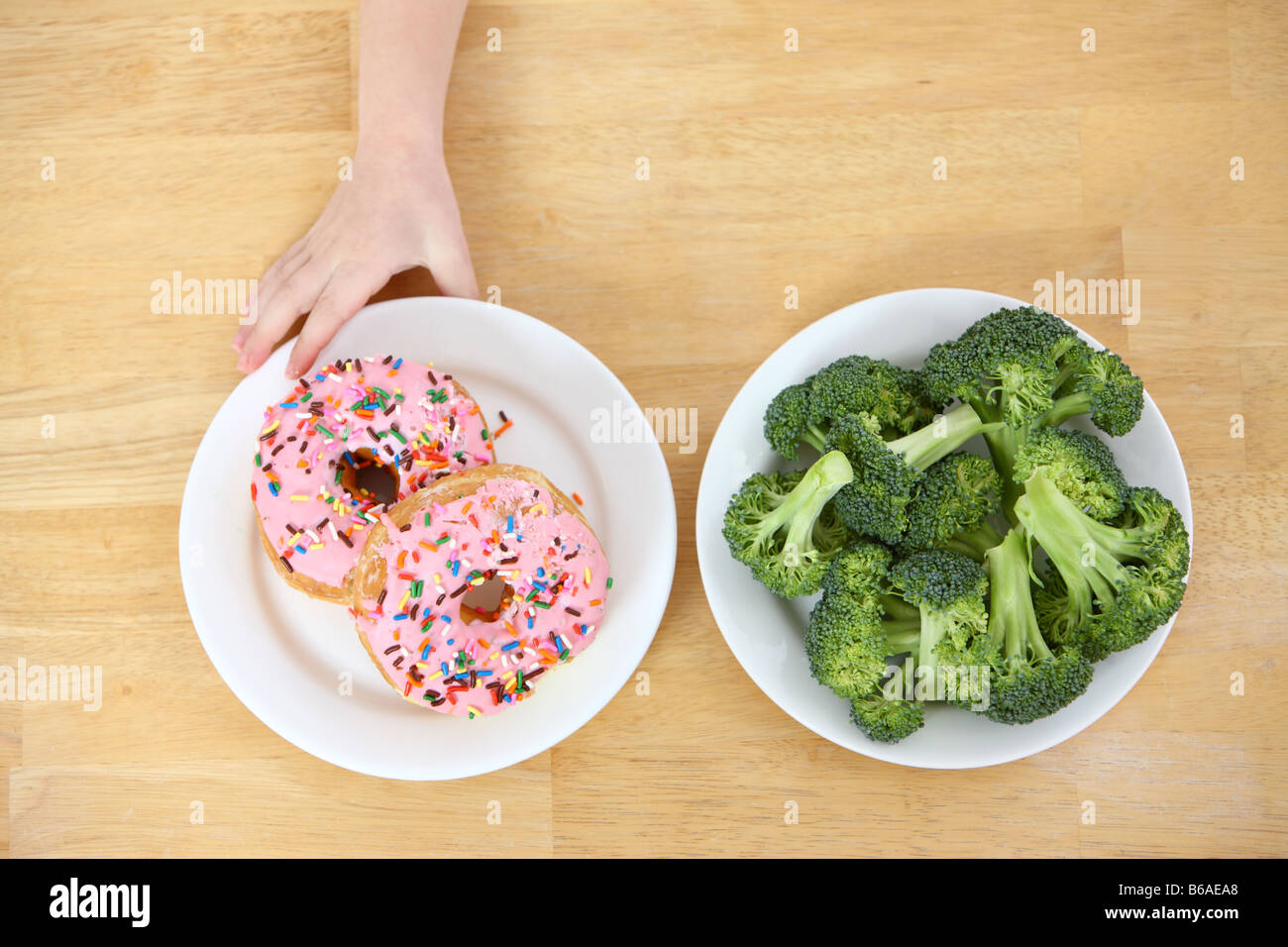 Child's hand reaching for doughnuts rather than broccoli Stock Photo