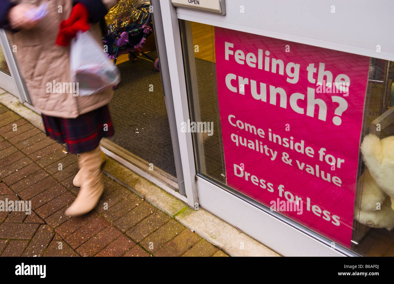FEELING THE CRUNCH, DRESS FOR LESS sign in window of charity shop