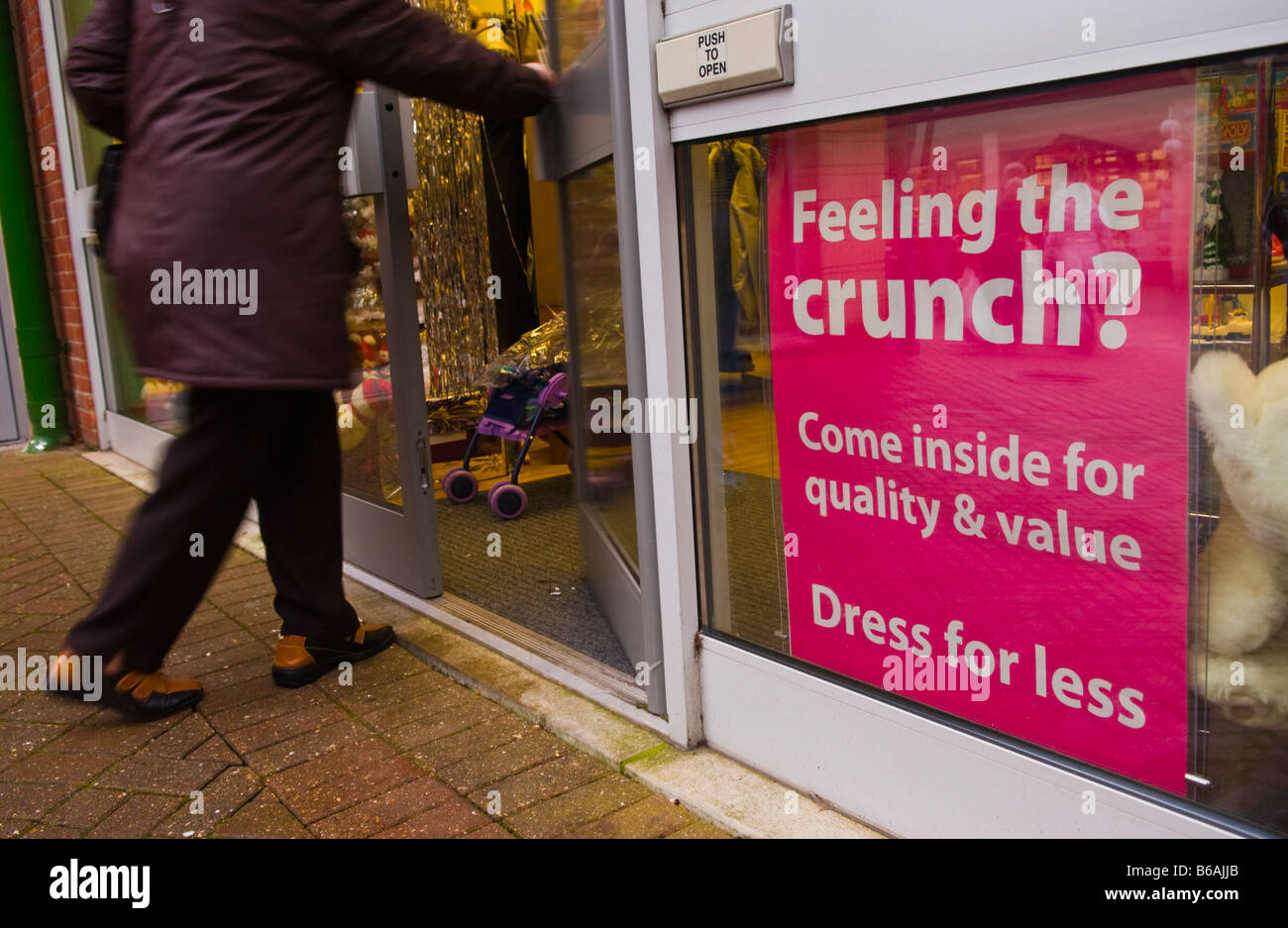 FEELING THE CRUNCH, DRESS FOR LESS sign in window of charity shop