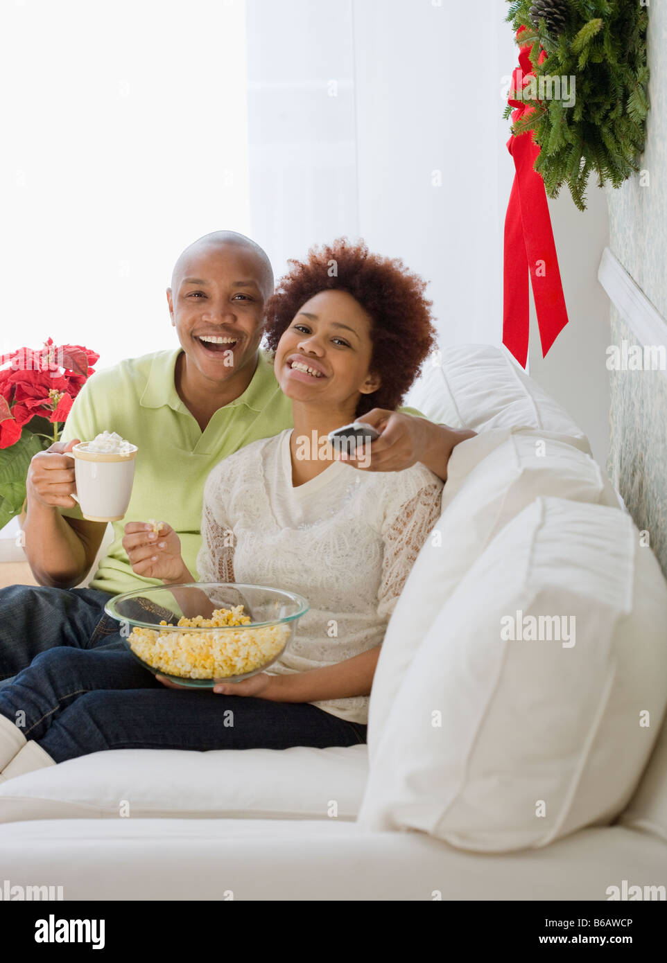 African couple watching television with popcorn and hot chocolate Stock Photo