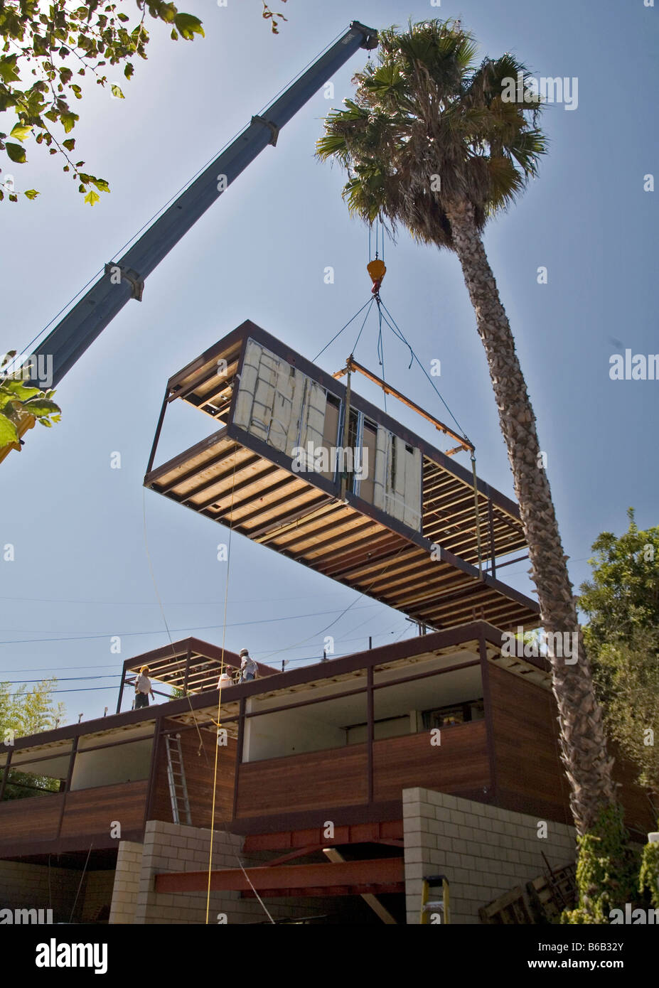 Prefab green architectural home being constructed. A crane is lifting a