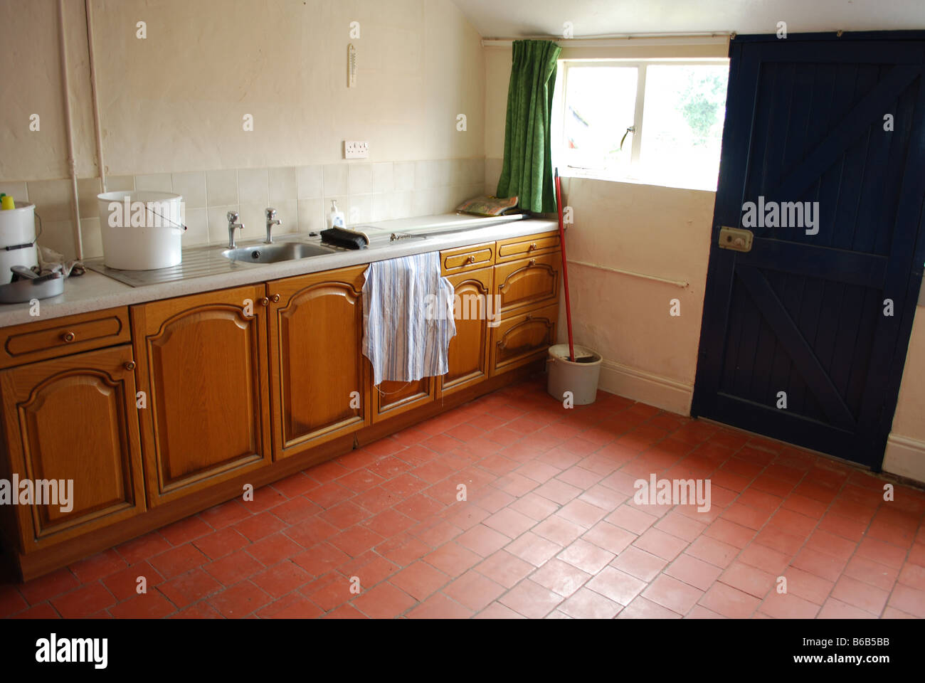 new kitchen units put in empty old farm house with a mop and bucket by a blue door, herefordshire, england Stock Photo