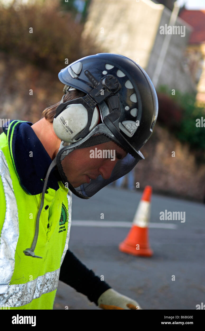 Tree surgeon wearing protective hard hat with ear defenders and mesh visor along with yellow Tree surgeon wearing protective hard hat with ear defenders and mesh visor along with yellow