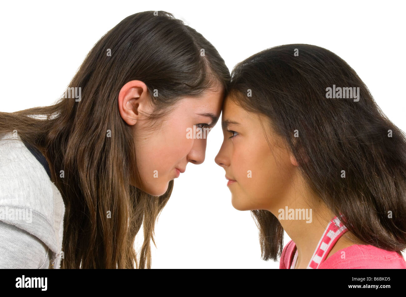 Horizontal portrait of two teenage sisters having an eyeball to eyeball confrontation during a fight against a white background. Stock Photo