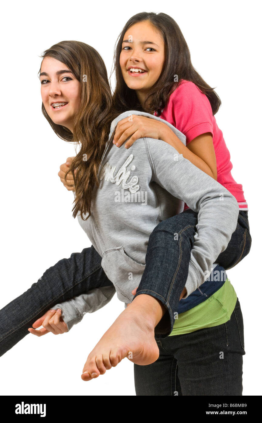 Vertical close up portrait of two teenage girls one giving the other a piggy back ride against a white background. Stock Photo