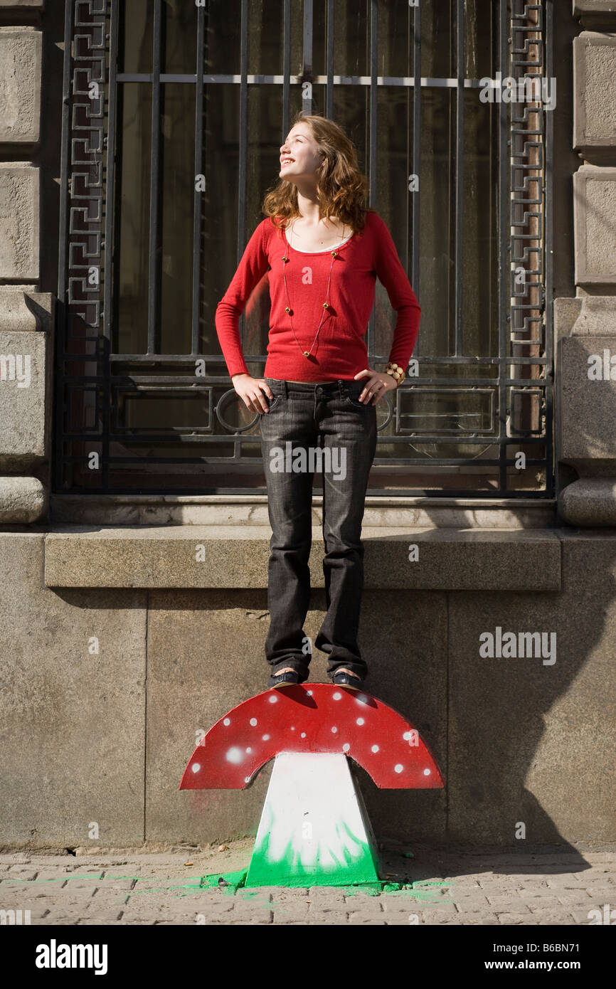 woman in red blouse and jeans standing on a mushroom made from iron plate Stock Photo