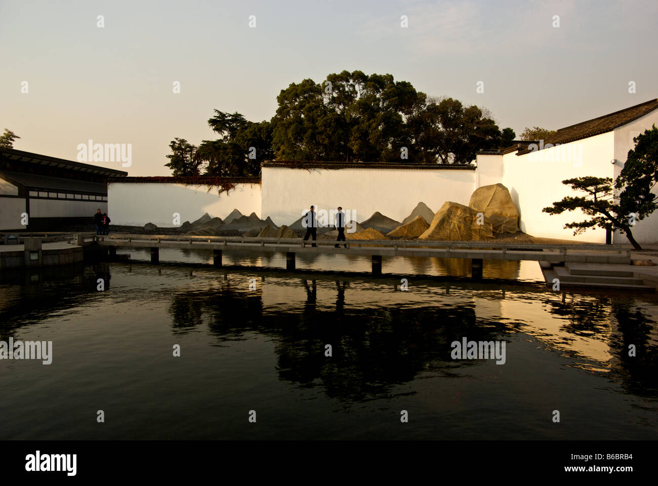 Reflecting pond with walkway and dramatic natural rock sculptures at dusk outside architect I M Pei designed New Suzhou Museum Stock Photo