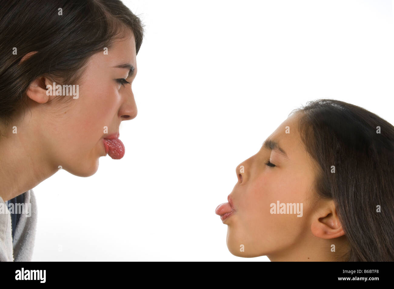 Horizontal close up portrait of two teenage sisters poking their tongues out during a fight against a white background Stock Photo